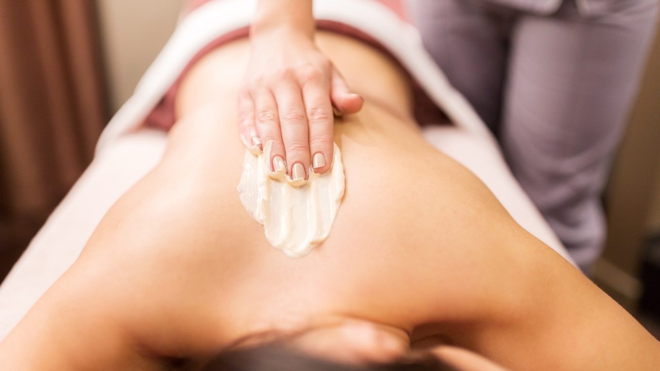 people, beauty, healthy lifestyle and relaxation concept - beautiful young woman lying and having back massage with cream at spa